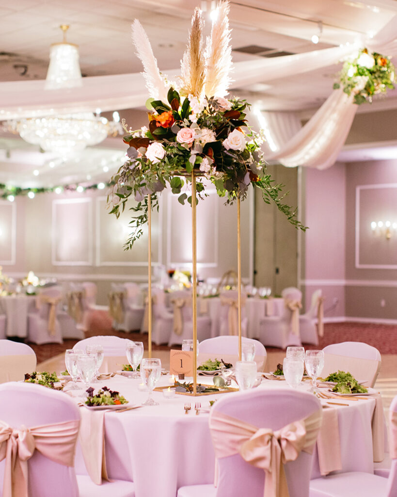 About 1 wedding reception venue with gold decor and tall floral centerpieces with pampas grass